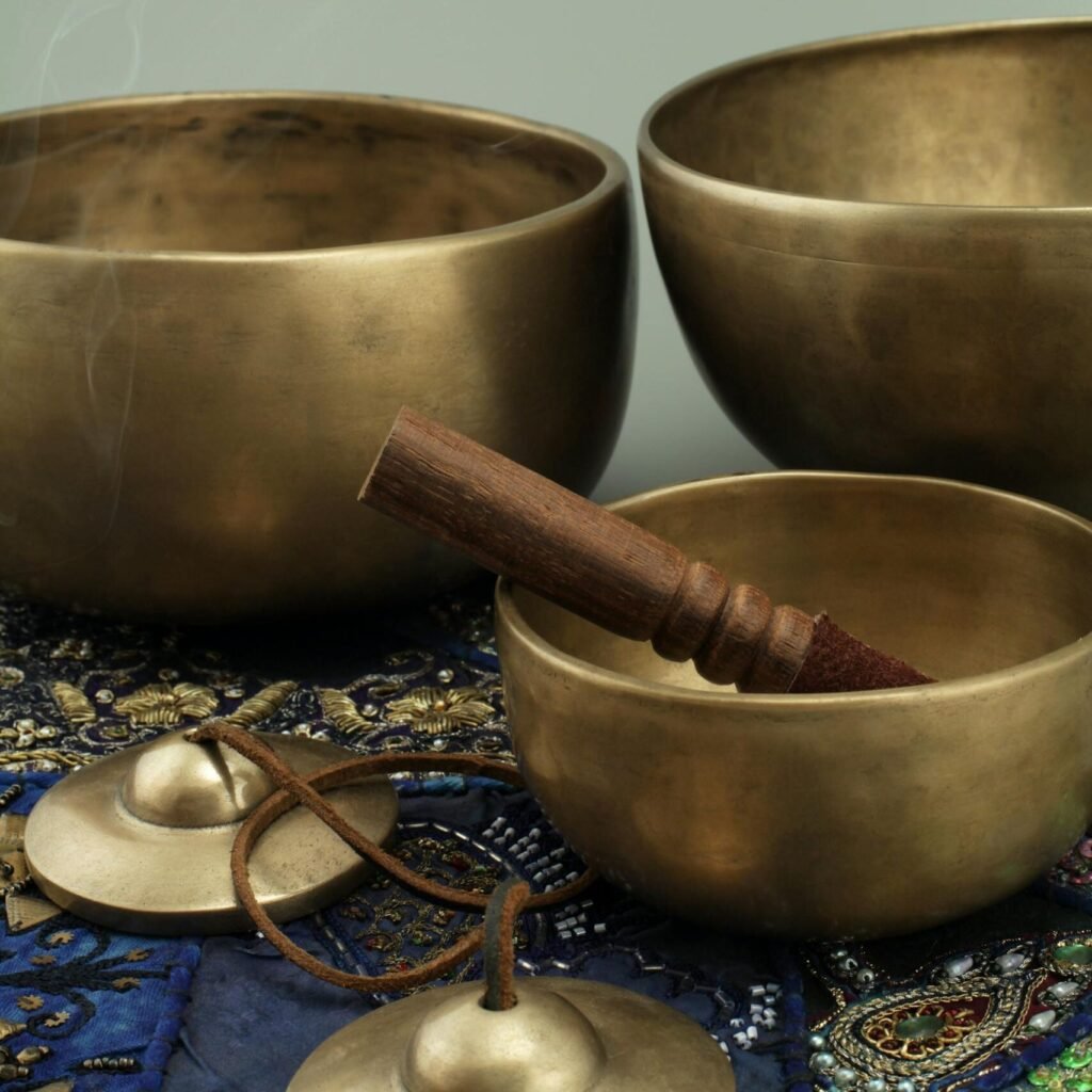 Close-up of antique bronze singing bowls with a wooden stick and smoke on a decorative cloth.
